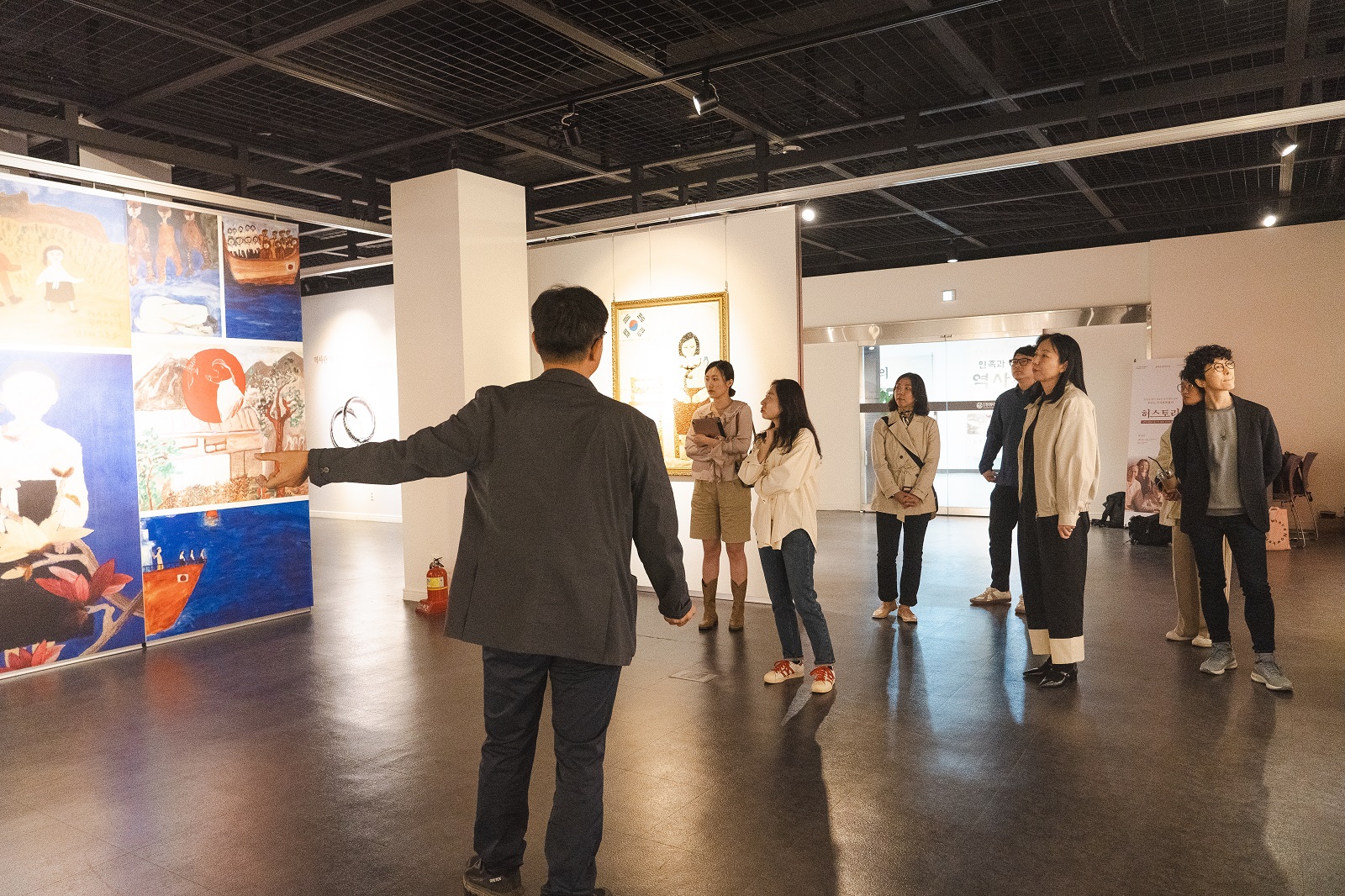 관람객들이 그림 패널 앞에 모여 전시 설명을 듣고 있는 모습이다.
