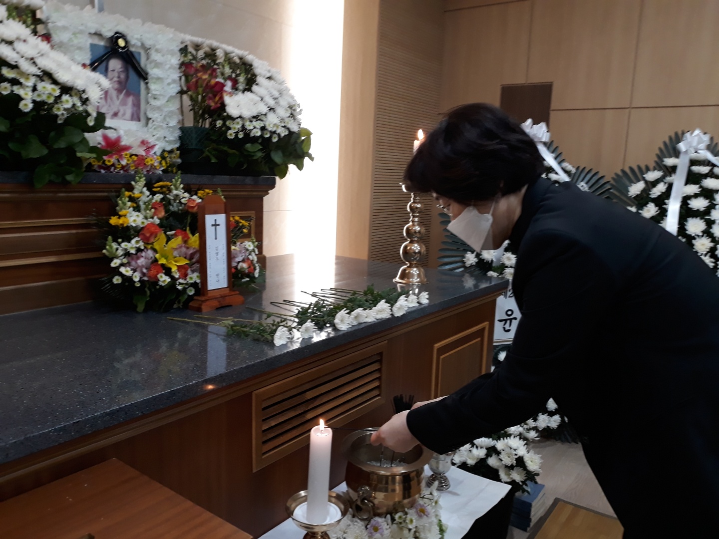 김양주 할머니의 영정과 십자가가 그려진 위패를 국화로 장식한 제단 앞에서, 검은 옷을 입은 조문객이 향을 피우고 있다.