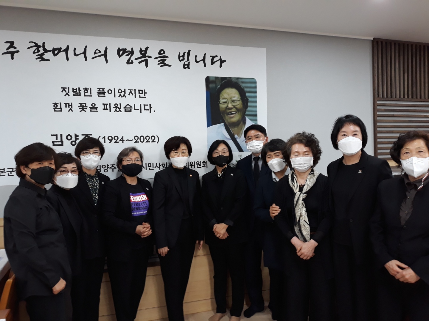 &ldquo;김양주 할머니의 명복을 빕니다. 짓밟힌 풀이었지만 힘껏 꽃을 피웠습니다.&rdquo;라고 적힌 현수막 앞에서 검은 옷을 입은 조문객 11명이 나란히 서서 찍은 사진이다.